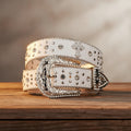 White rhinestone belt close-up with cross charm and studded strap, silver buckle